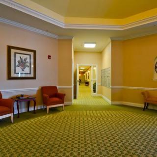 A warmly decorated hallway with carpeted flooring, featuring red chairs and artwork on the walls.