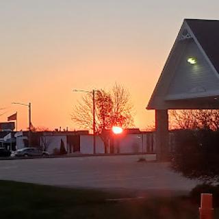 A beautiful sunset casting warm hues across the sky, with silhouettes of trees and a building in the foreground.
