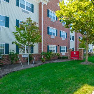 A residential apartment building with a brick exterior, surrounded by trees and a well-maintained lawn.