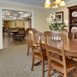 A cozy dining room with a wooden table and chairs, decorated with flowers and china plates.