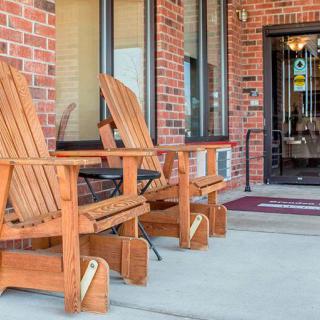 Wooden Adirondack chairs positioned outside the entrance of a brick building.