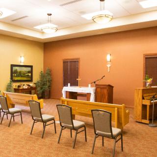 An interior view of a small chapel with chairs, a pulpit, and an altar.