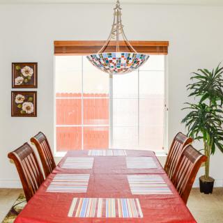 A well-organized dining room with a table set for six, featuring a red tablecloth and placemats, under a decorative chandelier.
