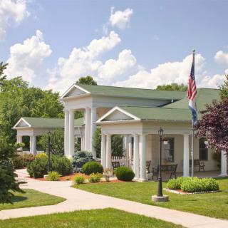 A building with a green roof and large columns, situated in a landscaped area with an American flag.