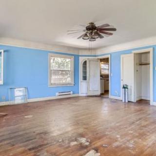 An empty room with wooden flooring, blue walls, and a ceiling fan.