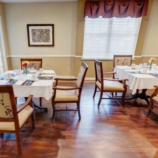 A cozy dining area with elegantly set tables and chairs, featuring hardwood floors and soft lighting.