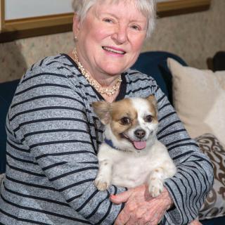 A smiling woman holding a small dog indoors.
