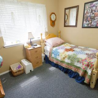 A cozy and well-lit bedroom featuring a neatly made bed, nightstand with a lamp, and personal touches like photos on the wall.