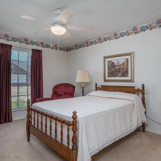 A cozy bedroom with a wooden bed frame, red upholstered chair, floor lamp, and window with red curtains.