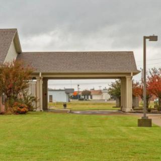 A view of a building with an archway, surrounded by a neatly mowed lawn and trees under a cloudy sky.
