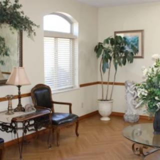 A cozy living room with a wooden chair, glass table, and decorative plants by the window.