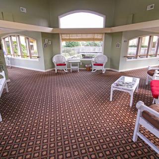 A spacious living room with large windows, wicker chairs, and a patterned carpet.