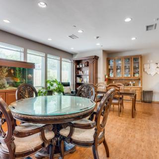 A stylish dining room with a round glass table, elegant chairs, and wooden flooring, complemented by a fish tank and decorative plants.