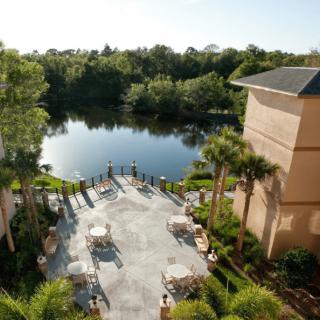 A serene view of a hotel patio overlooking a tranquil lake surrounded by lush greenery.