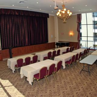 A conference room setup with rows of tables and chairs facing a stage, illuminated by a chandelier.