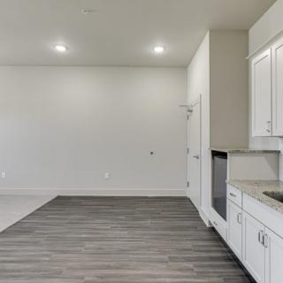 A modern, minimalist kitchen with white cabinets and wood flooring.