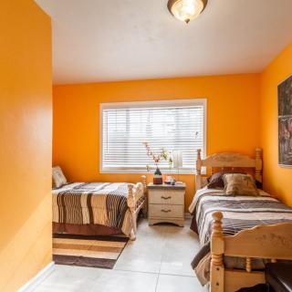 A cozy bedroom with vibrant orange walls, featuring two wooden beds and a window letting in natural light.