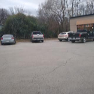 A view of a parking lot with several parked vehicles and trees in the background under a cloudy sky.