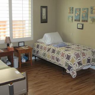 A cozy bedroom featuring a single bed with patterned bedding, wooden flooring, and wall decorations.