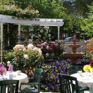 A charming outdoor dining area surrounded by vibrant flowers and a fountain.