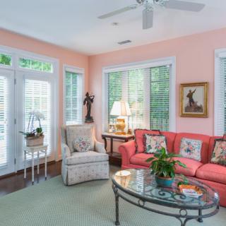 A cozy living room with a coral sofa, patterned armchair, and large windows allowing natural light to fill the space.