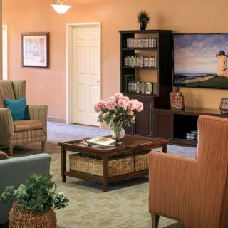 A cozy living room with comfortable seating, a coffee table adorned with flowers, and a bookshelf alongside a scenic painting.