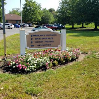 An outdoor sign indicating directions for parking and visitor entrance, surrounded by a landscaped area with flowers.