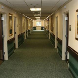 A long, carpeted hallway with multiple doors on either side, illuminated by overhead lighting.
