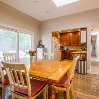 A cozy dining area with a wooden table and chairs, adjacent to a kitchen featuring warm wood cabinetry. Natural light streams in through large windows and a skylight.