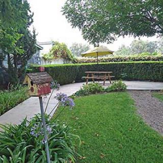 A serene backyard garden featuring a birdhouse, lush greenery, and a picnic table shaded by an umbrella.