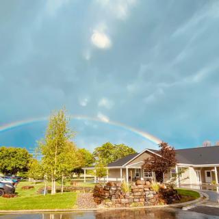 A beautiful rainbow arches over a house and garden on a cloudy day.