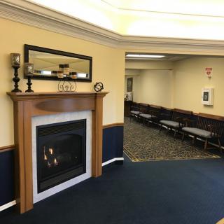 A cozy interior featuring a fireplace and a mirror, adjacent to a meeting room with chairs lined up.