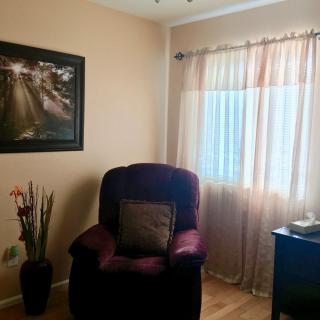 A cozy living room corner with a plush armchair, soft curtains, and wall art.