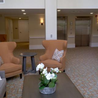 A cozy lobby area with comfortable chairs, a small table, and elevators in the background.