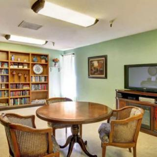 A cozy library room with a round table, chairs, bookshelf, and television.