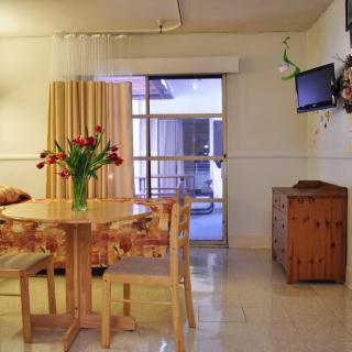 A cozy dining area in an apartment featuring a wooden table with chairs, a television mounted on the wall, and a vase of flowers as a centerpiece.