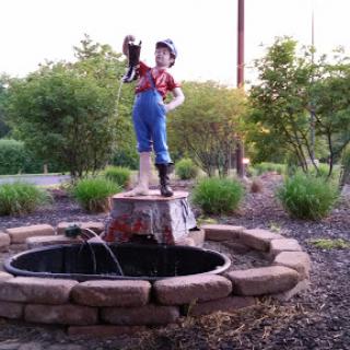 A charming garden fountain featuring a statue of a boy holding a bucket, surrounded by lush greenery.