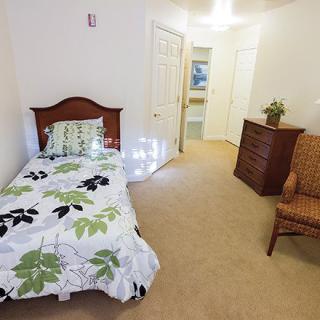 A cozy bedroom with a single bed, dresser, and armchair.