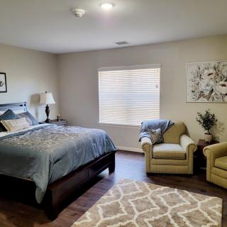 A cozy bedroom with a bed, two armchairs, and a large window letting in natural light.