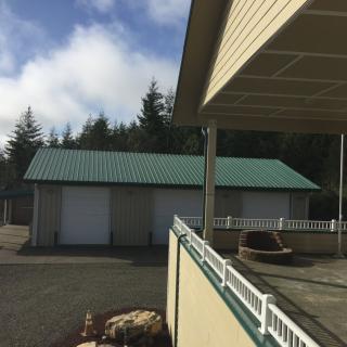 A green-roofed garage adjacent to a house with a sunny outdoor setting and trees in the background.