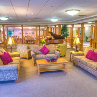 A cozy lounge area featuring several sofas with colorful pillows, a central coffee table, and a piano in the background.