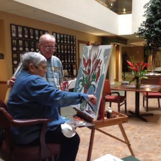 Two elderly individuals engaging in a painting activity indoors.