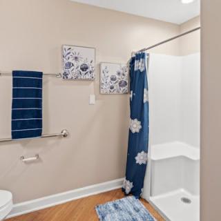 A modern bathroom with blue and white dcor, featuring a shower with a floral curtain, coordinating towels, wall art, and a bath mat.