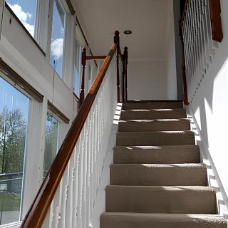 A staircase with carpeted steps and wooden railings, illuminated by natural light from large windows.