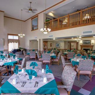 A well-lit dining area with neatly arranged tables and chairs, featuring teal accents and a loft above.