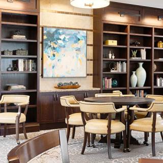 A modern library interior with bookshelves, a table and chairs, and abstract artwork.