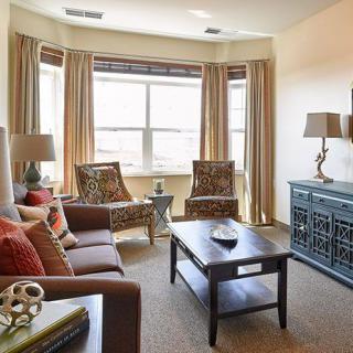 A cozy and beautifully decorated living room with a sofa, patterned chairs, and natural light streaming in through the windows.