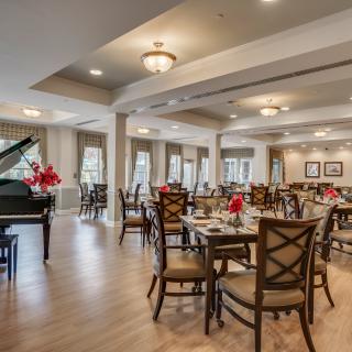 An elegant dining room with neatly arranged tables and a grand piano.
