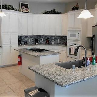 A modern kitchen with white cabinets, granite countertops, an island, and built-in appliances.