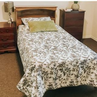 A cozy bedroom featuring a single bed with floral bedding, accompanied by a wooden nightstand and dresser.